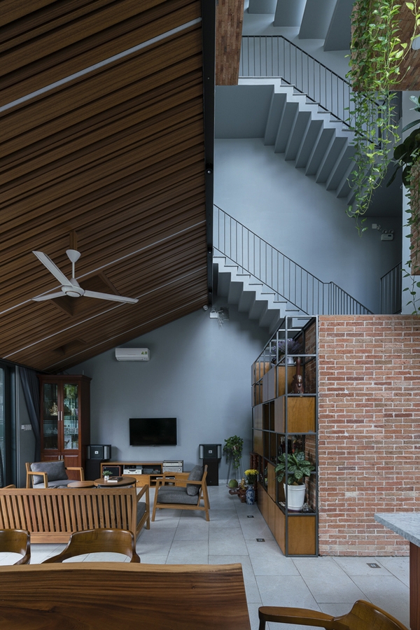 Phía trên phòng khách là một trần gỗ dốc gợi nhắc mái nhà dân gian. Chất liệu gỗ và gạch trần gợi cảm giác gần gũi, ấm áp.