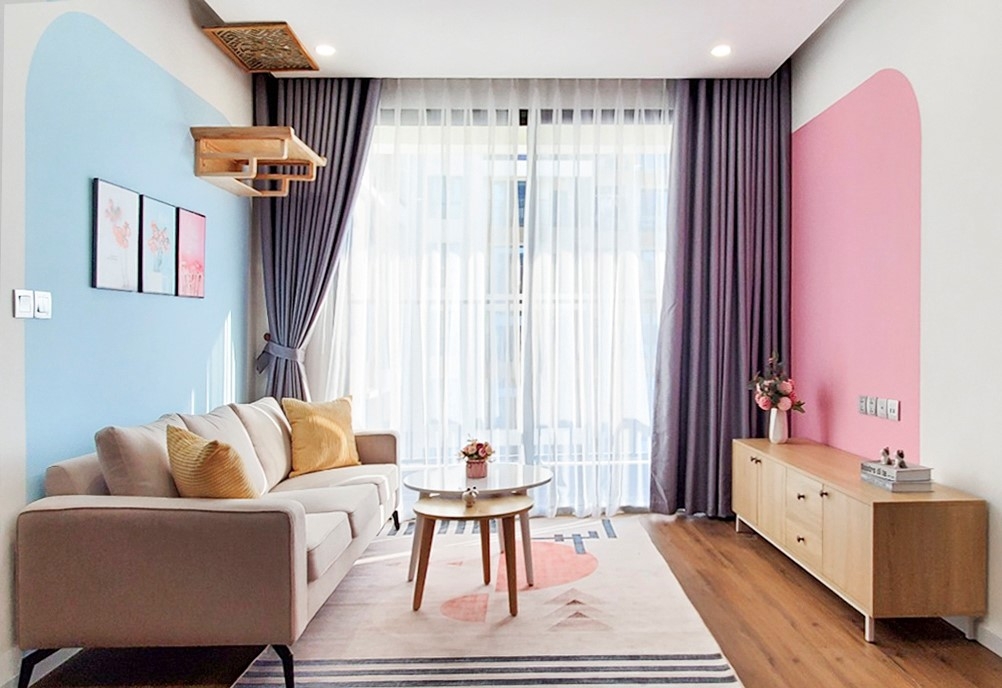 Sofa màu ghi nhạt ăn ý với rèm cửa, bức tường với những mảng màu hồng cánh sen và xanh da trời tưởng đối lập nhưng mang lại cảm giác dễ chịu, trẻ trung khi bước vào nhà.