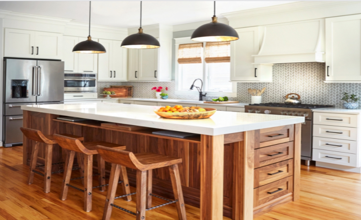 Căn phòng bếp tại bang Maryland, Mỹ, này có nhiều chi tiết thiết kế hấp dẫn. Những tủ và quầy bếp dài màu trắng tạo cảm giác nhẹ nhàng và thoáng đãng trong khi tấm ốp gốm màu xám tạo thêm sự chuyển động và hoa văn. Quầy bếp làm bằng gỗ óc chó được thiết kế tỉ mỉ, tinh tế là trung tâm của căn bếp. Một kệ mỏng bên dưới mặt bàn bằng thạch anh tạo không gian để laptop và các công cụ khác để làm việc tại nhà. Ổ cắm điện được bố trí phía sau kệ cho phép gia chủ sạc các thiết bị, trong khi ngăn kéo để giấy và các vật dụng khác.