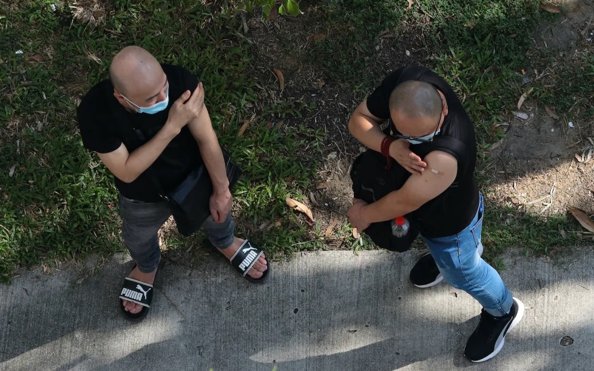 Hai nam giới đợi bên ngoài một cơ sở y tế sau khi được tiêm chủng Covid-19 ở Singapore vào tháng 6/2021. Ảnh: NurPhoto.