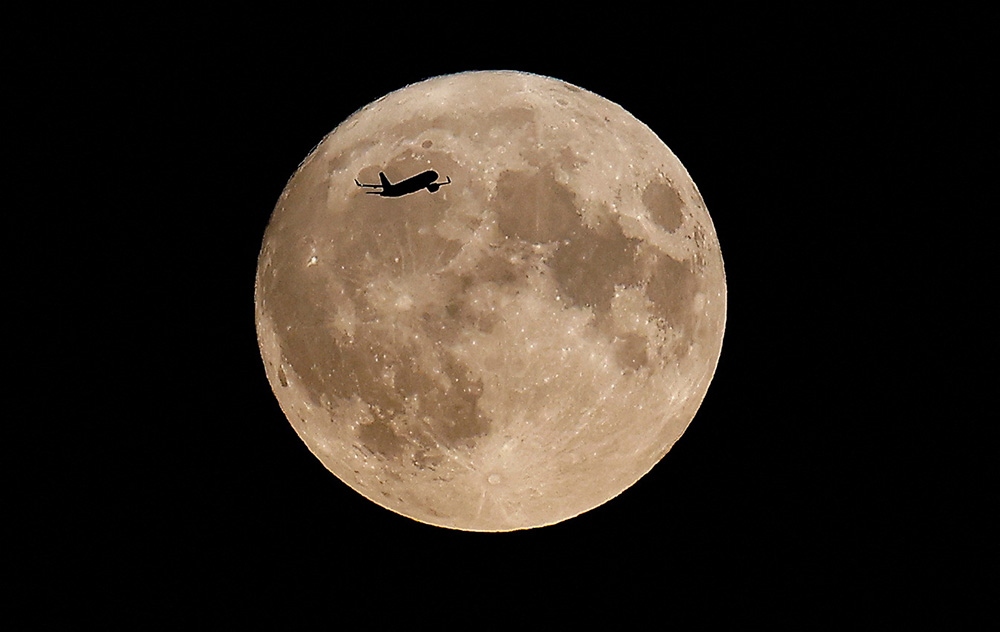 Một chiếc máy bay bay phía trước siêu "Trăng Xanh" tối 31/8. Ảnh: Reuters