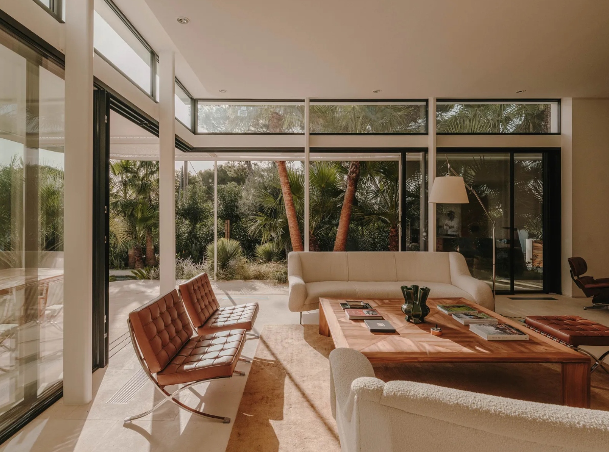 Phòng khách là sự kết hợp giữa những món đồ nội thất cổ điển và hiện đại. Bộ ghế bành trông cực kỳ hòa hợp với chiếc bàn gỗ tếch đồng màu, kết hợp với những khung kính lớn, khiến bạn như hòa mình vào thiên nhiên dù vẫn đang ở trong nhà. 