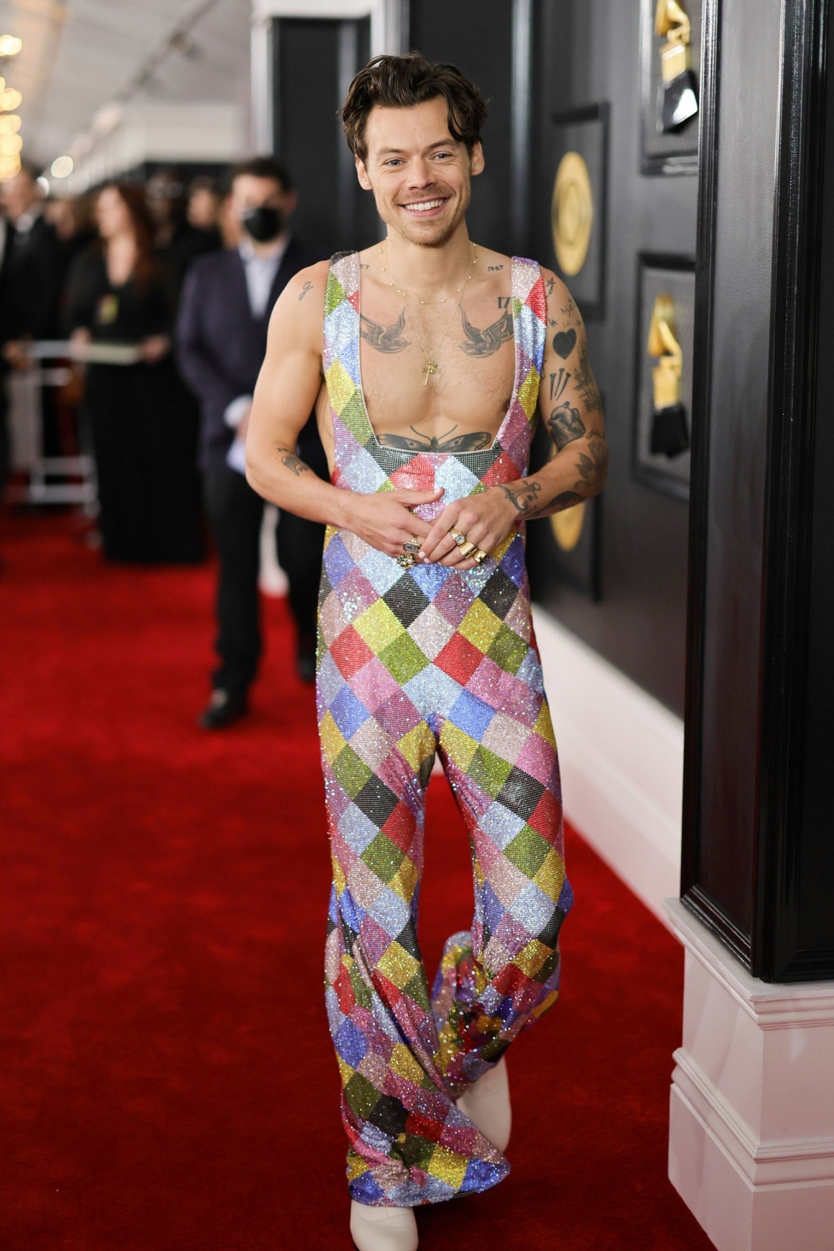 Trang phục của Harry Styles tại lễ trao giải Grammy 2023 được nhắc đến nhiều nhất vào thời điểm diễn ra sự kiện. Bộ đồ gợi nhớ đến phong cách áo liền quần theo phong cách rock cổ điển lòe loẹt trong những năm 70.
Giọng ca “Watermelon Sugar” bước trên thảm đỏ trong bộ trang phục yếm in họa tiết harlequin. Giữ vững tinh thần về thời trang phi giới tính của mình, Harry Styles không ngần ngại diện lên thảm đỏ bộ jumpsuit cực kỳ bắt mắt của EGONlab. Bộ đồ có phom dáng mềm mại, phần ngực vuông khoét sâu càng trở nên nổi bật hơn với những ô màu cầu vồng sặc sỡ và được đính kết thủ công pha lê Swarovski của thương hiệu thời trang Pháp EgonLab
