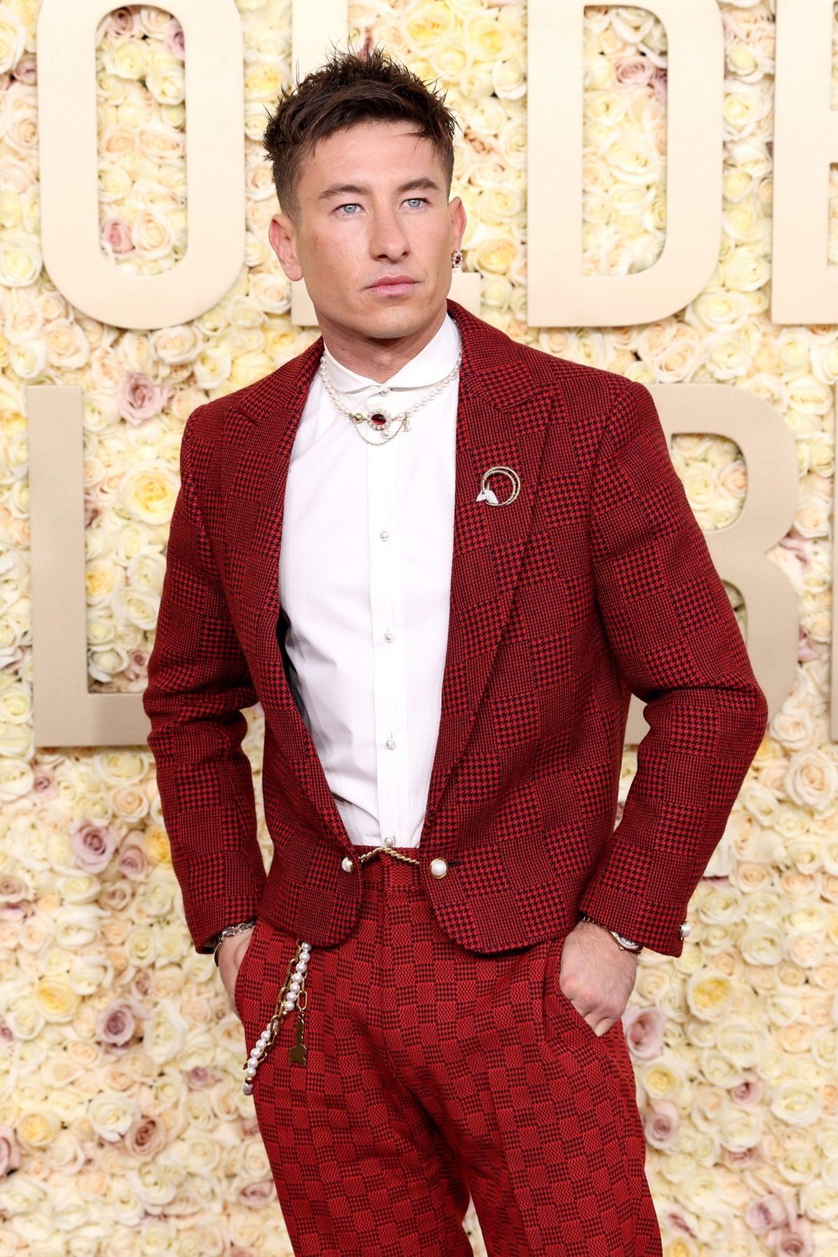 Barry Keoghan diện chiếc áo khoác len dạ màu đỏ có họa tiết Damier đặc trưng của Louis Vuitton. Chiếc quần ca-rô màu đỏ từ bộ sưu tập Xuân-Hè 2024 của hãng, hoàn chỉnh với dây chuyền thắt lưng ngọc trai, vòng cổ, bông tai và một chiếc trâm cài Tiffany &amp; Co.