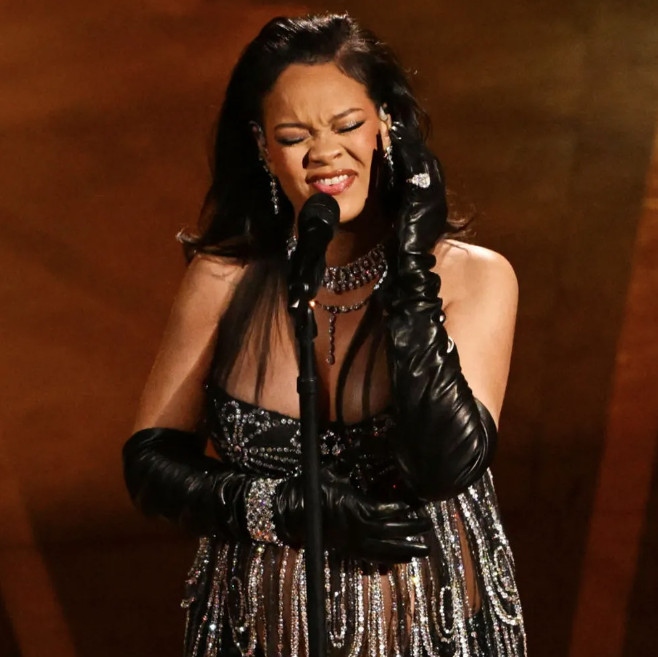 Rihanna trong thiết kế riêng của Maison Margiela.
Tại buổi biểu diễn Oscar, nữ ca sĩ đã xuất hiện trên sân khấu trong một dàn đồng phục đầy mê hoặc khiến khán giả phải kinh ngạc. Cô tỏa sáng sự sang trọng và tinh tế trong chiếc váy màu đen được trang trí bằng một loạt pha lê lấp lánh, dây đai lưới mỏng tạo thêm nét quyến rũ. Kết hợp hoàn hảo với chiếc quần đen có họa tiết hoa màu vàng tinh xảo, vẻ ngoài toát lên sự pha trộn hoàn hảo giữa sự quyến rũ và góc cạnh.
Được thiết kế riêng bởi Maison Margiela dưới sự chỉ đạo có tầm nhìn của John Galliano, mọi chi tiết của bộ trang phục đều được tuyển chọn tỉ mỉ để nâng cao sự hiện diện của cô trên sân khấu. Hoàn thiện bộ trang phục là đôi giày cao gót màu đen bóng bẩy, găng tay opera bằng da và một loạt đồ trang sức kim cương rực rỡ, bao gồm dây chuyền nhiều lớp, chiếc vòng tay nổi bật đeo trên găng tay và đôi bông tai hình giọt kim cương tính xảo.