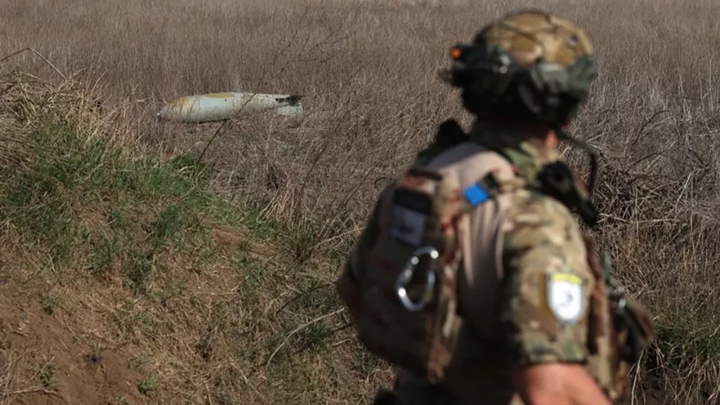 Một binh sĩ đi ngang qua một quả bom FAB-500 chưa nổ của Nga trên cánh đồng gần làng Ocheretyne, cách Avdiivka không xa. Ảnh: AFP