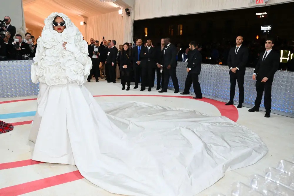 Rihanna đến Met Gala 2023 một cách đầy thời trang trong chiếc váy trắng phối cùng áo khoác ngoài. Trong buổi dạ tiệc "Karl Lagerfeld: A Line of Beauty", Rihanna mặc chiếc váy Valentino Haute Couture đặt làm riêng. Chiếc váy có vạt áo vừa vặn khoe bụng bầu với hình hoa cầu kỳ ở giữa. Chân váy dài thướt tha như một đoàn tàu dài. Rihanna hoàn thiện bộ trang phục với một chiếc áo khoác có mũ trùm đầu đính những bông hoa ngoại cỡ, găng tay hở ngón và kính râm có gắn lông mi.