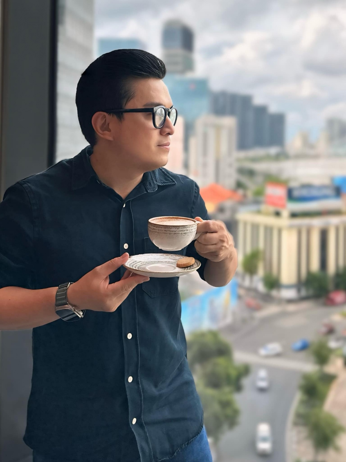 Lam Trường thảnh thơi vừa uống trà, vừa ngắm thành phố từ trên cao. “Ngắm thành phố từ trên cao, tách trà chiều, trong lòng lại le lói ánh nắng nhẹ qua tim”, nam ca sĩ tâm sự. (Nguồn: FBNV)