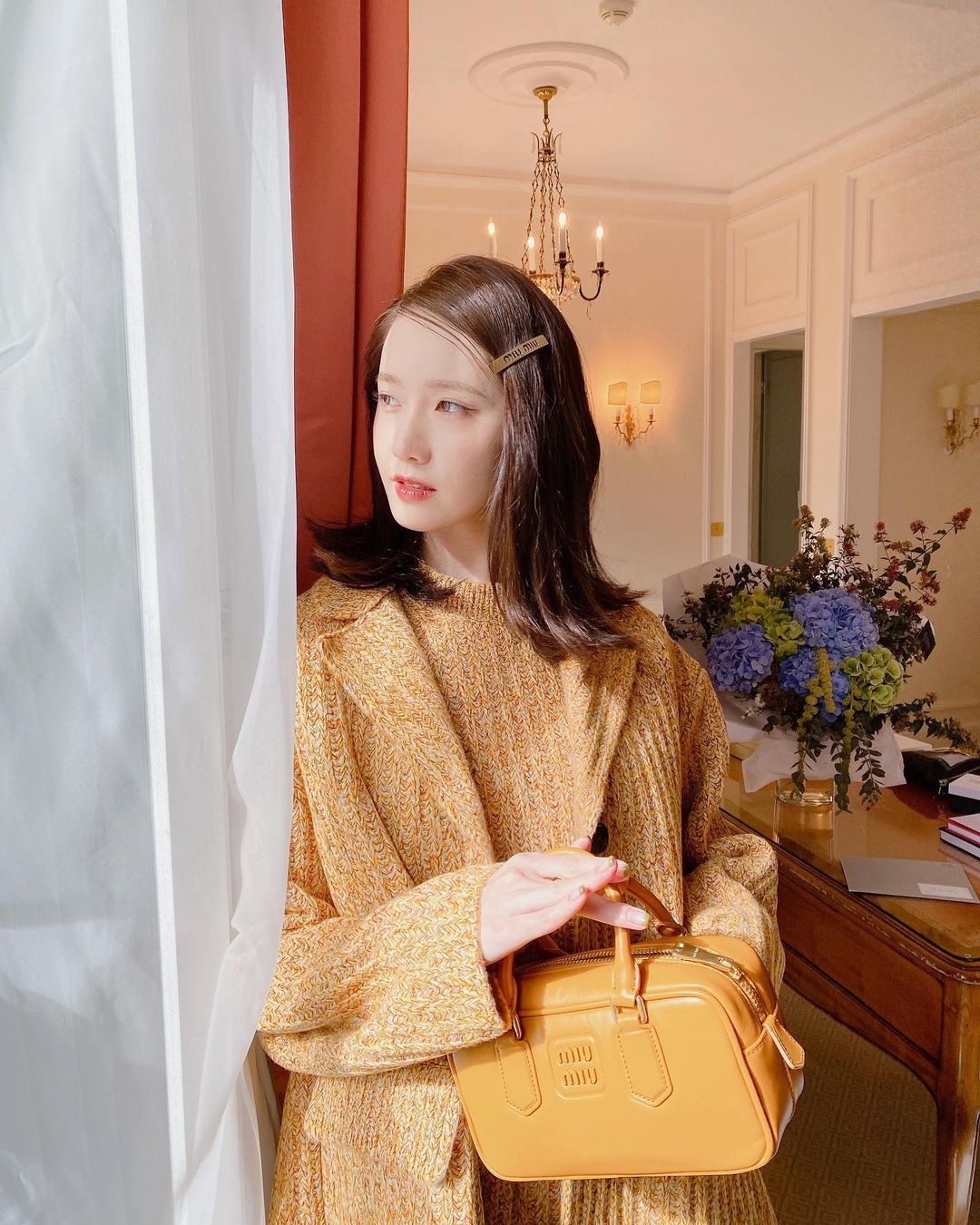 Yoona hóa nàng thơ đầy ngọt ngào khi đeo chiếc túi Beau màu vàng của Miu Miu kết hợp với áo len cùng tông màu. Cô nàng còn tăng thêm phần nữ tính khi đeo chiếc cặp tóc cũng của thương hiệu Miu Miu. Túi da Beau của Miu Miu có giá khoảng 3.850 USD.