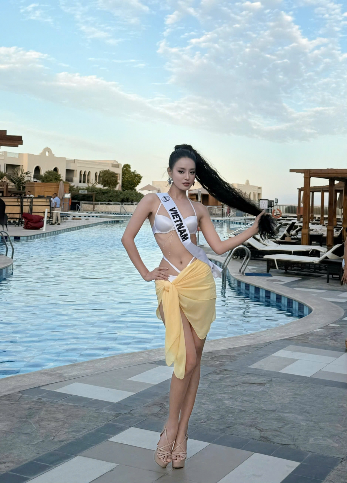 Á hậu Khánh Linh đã chuẩn bị trang phục bikini trắng theo yêu cầu của Ban tổ chức cuộc thi. Thiết kế ấn tượng đến từ NTK Khang Trịnh, tôn lên trọn vẹn hình thể và đường cong quyến rũ của nàng hậu.