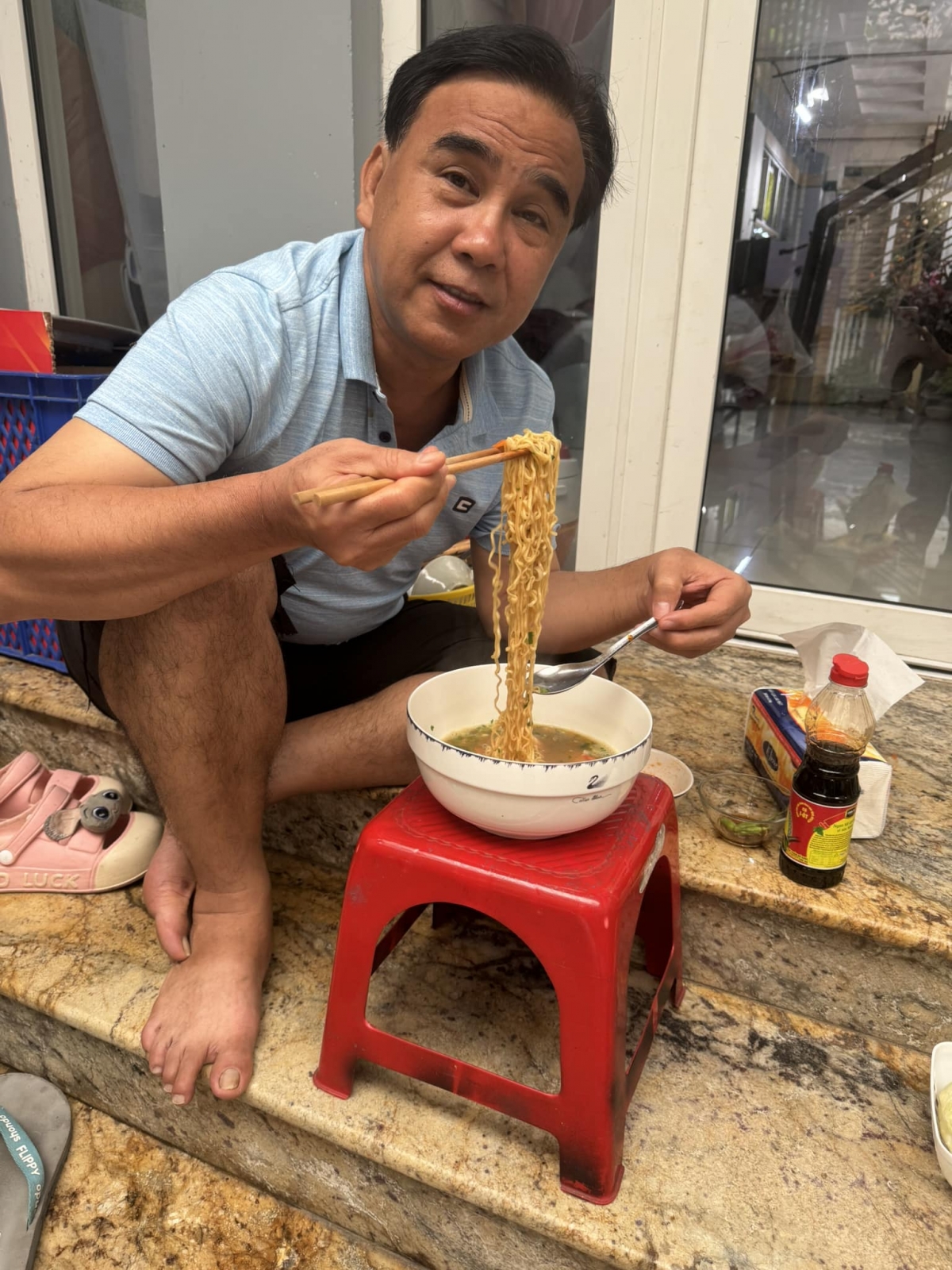 Quyền Linh đăng ảnh ngồi ăn mì tôm. Trong ảnh, anh ăn mặc giản dị, mộc mạc với chiếc quần đùi và áo phông đơn giản. (Nguồn: FBNV)