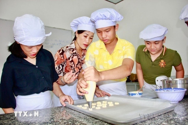 Giáo viên hướng dẫn trẻ khuyết tật đánh bột làm các loại bánh tại Trung tâm Bảo trợ xã hội tỉnh Khánh Hòa, nhằm giúp các em có nghề và việc làm sau khi được đào tạo. (Ảnh: Phan Sáu/TTXVN)