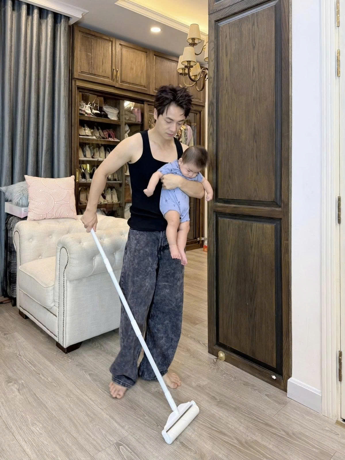 Ca sĩ Đăng Khôi vừa bế con vừa làm việc nhà. (Nguồn: FBNV)