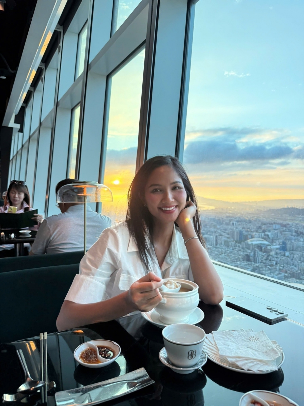 Hoa hậu H'Hen Niê dùng bữa tại tòa tháp 101 ở Đài Loan (Trung Quốc). Cô bày tỏ: “Được ngắm cảnh hoàng hôn tuyệt đẹp, ngắm mọi khía ánh sáng khi đang buông xuống xen kẻ ánh chiều tà qua các tòa nhà, rất huyền ảo, lãng mạn và cực đã mắt”. (Nguồn: FBNV)