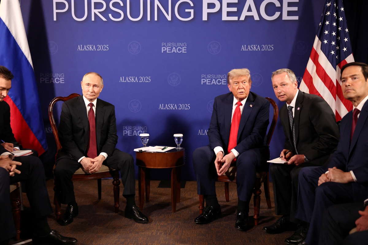 Tổng thống Mỹ Trump và người đồng cấp Nga Putin ngồi cạnh nhau tại một căn phòng ở căn cứ Elmendorf-Richardson, phía sau là phông nền có dòng chữ "Theo đuổi hòa bình".