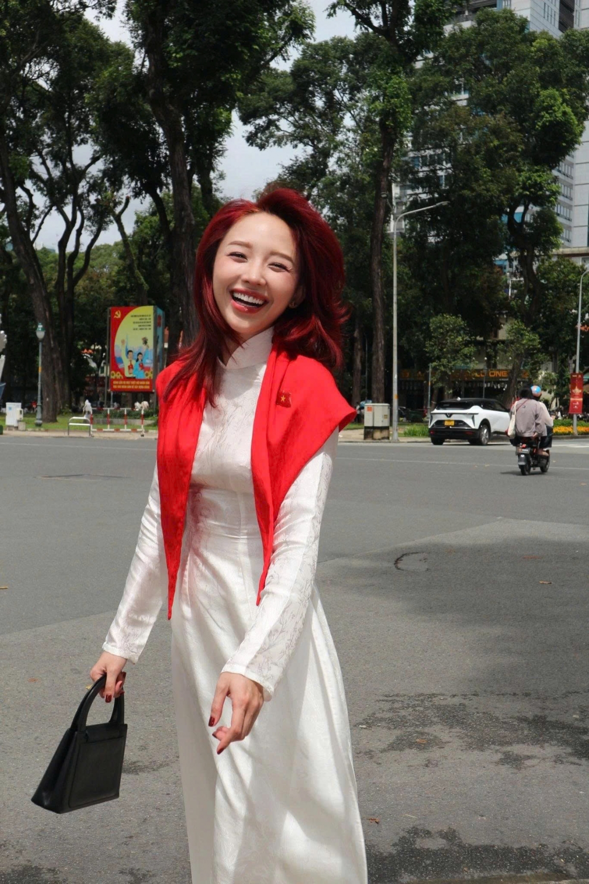 Ca sĩ Tóc Tiên xuất hiện rạng rỡ trong tà áo dài trắng kết hợp khăn choàng đỏ, tạo nên điểm nhấn nổi bật giữa khung cảnh đường phố.
