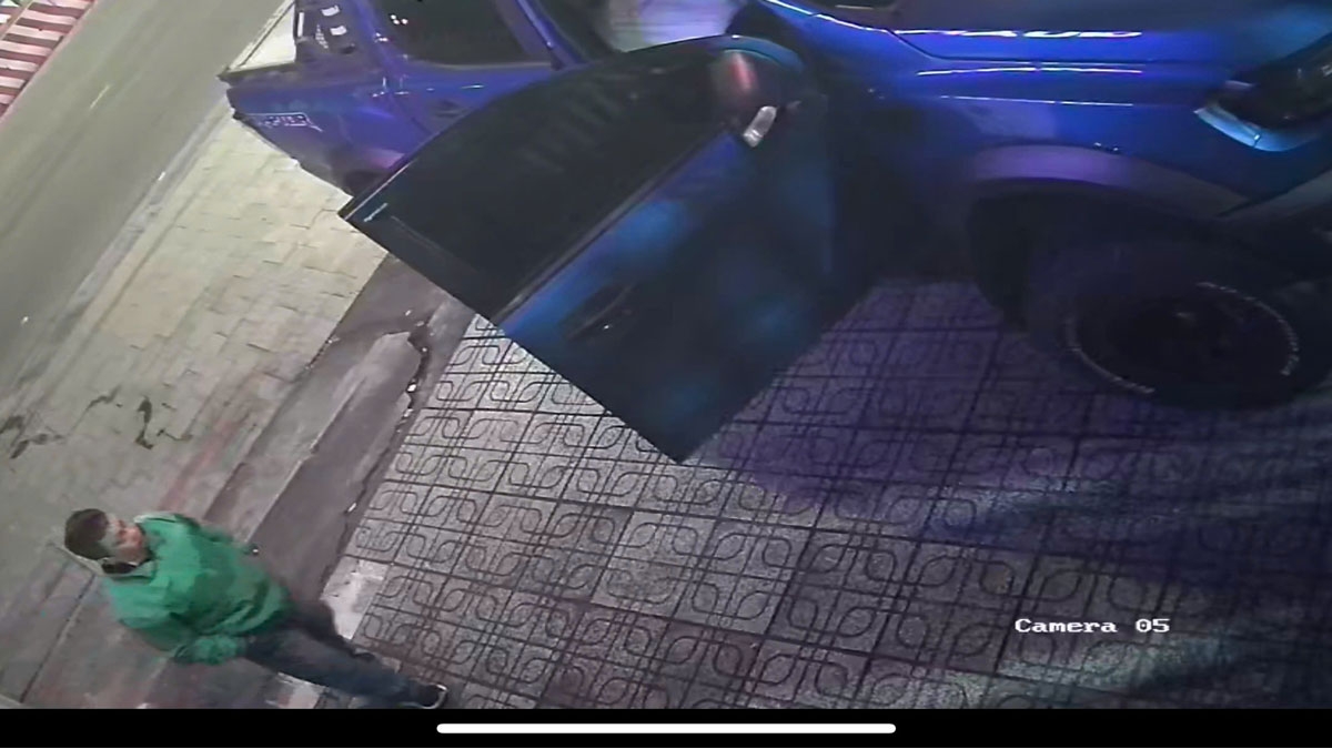 Người đàn ông mặc áo xanh đi lại gần xe ô tô 