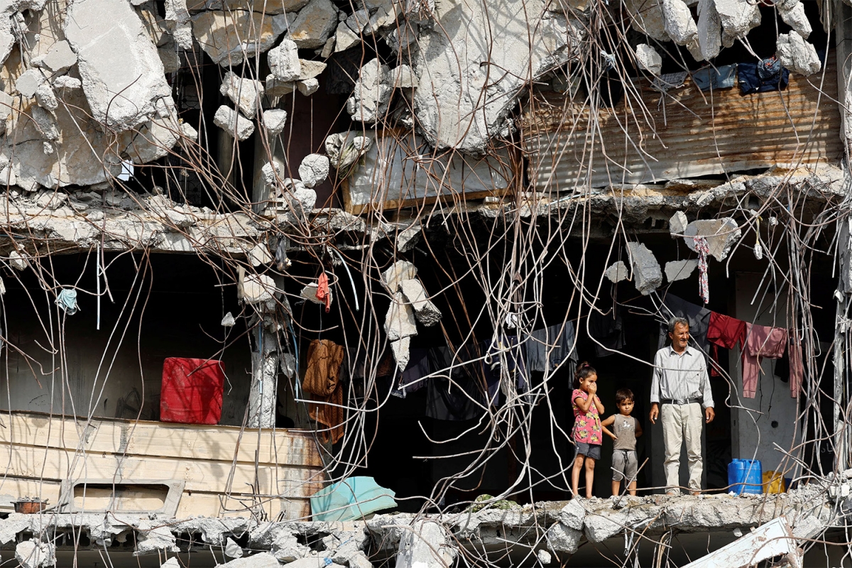 Một người đàn ông Palestine cùng các em nhỏ đứng bên tòa nhà hư hại nặng, trong thời gian lệnh ngừng bắn giữa Israel và Hamas có hiệu lực tại Thành phố Gaza, ngày 2/11/2025. Ảnh: Reuters