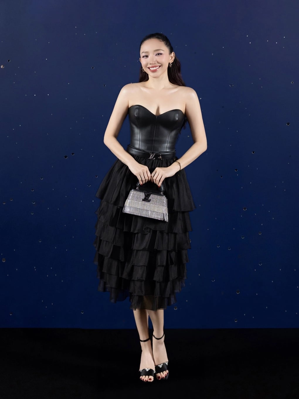 Tóc Tiên mặc đầm đen pha trộn chất liệu da cá tính và chiffon xếp tầng mềm mại, kết hợp túi Louis Vuitton Capucines tua rua lấp lánh khi tham dự một sự kiện thời trang. Phom váy cúp ngực siết eo giúp mỹ nhân 36 tuổi làm nổi bật vòng một đầy đặn.