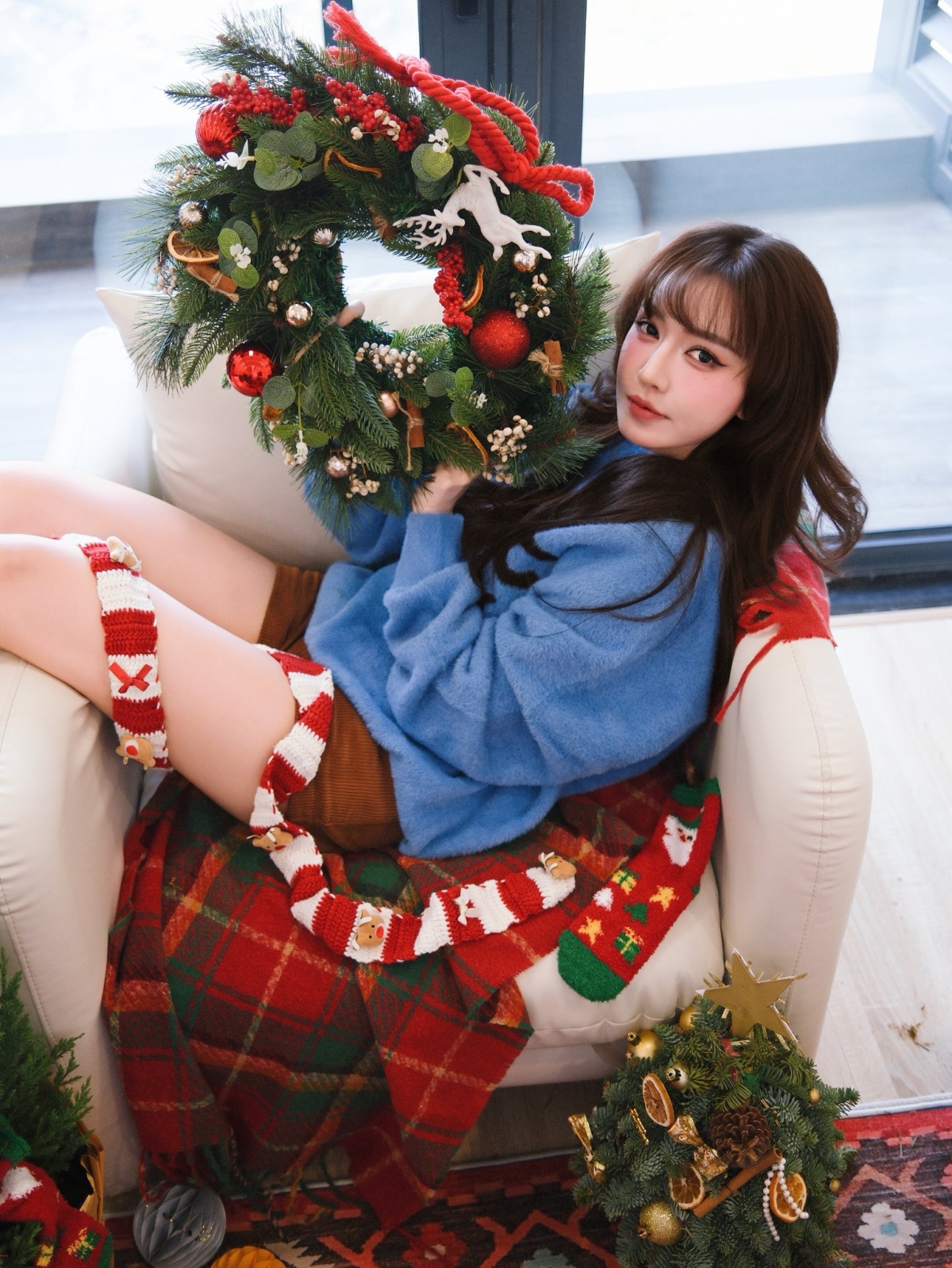 Ca sĩ Bích Phương chụp ảnh trong không gian trang trí đậm chất Giáng sinh. Nữ ca sĩ diện áo len xanh dáng rộng, quần ngắn tông nâu, tạo cảm giác ấm áp.