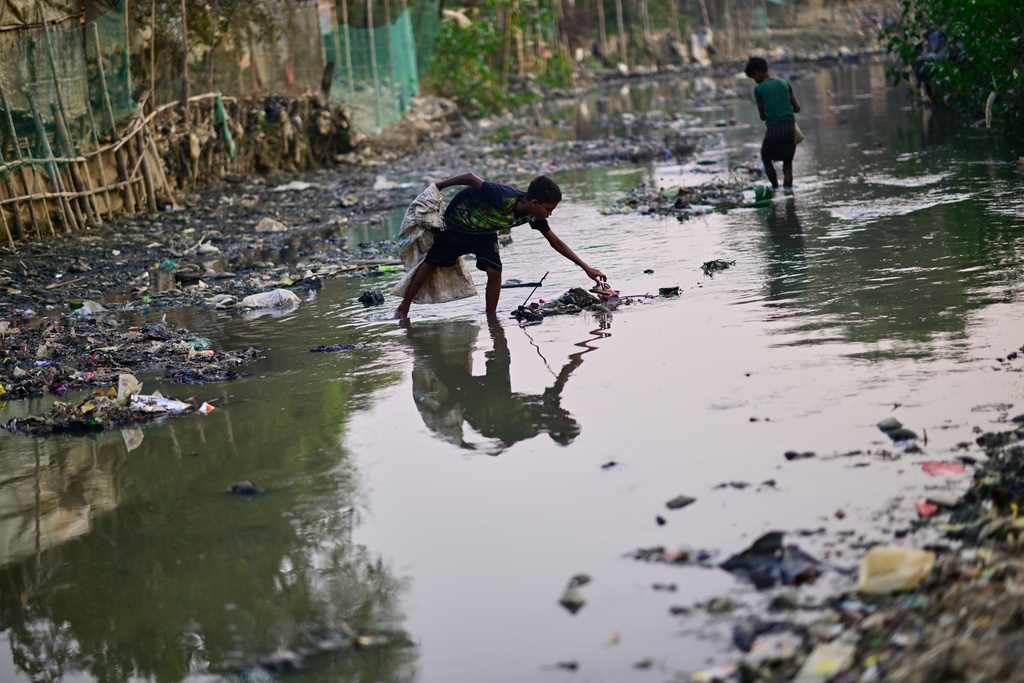 Cậu bé Rahamot Ullah, một người tị nạn Rohingya 13 tuổi, đang thu gom rác thải nhựa từ một kênh thoát nước bên trong trại tị nạn.