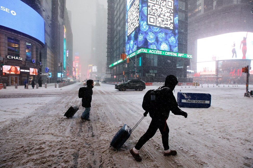 Hành khách kéo hành lý đi bộ giữa trời tuyết rơi tại Quảng trường Thời đại, New York ngày 25/1.