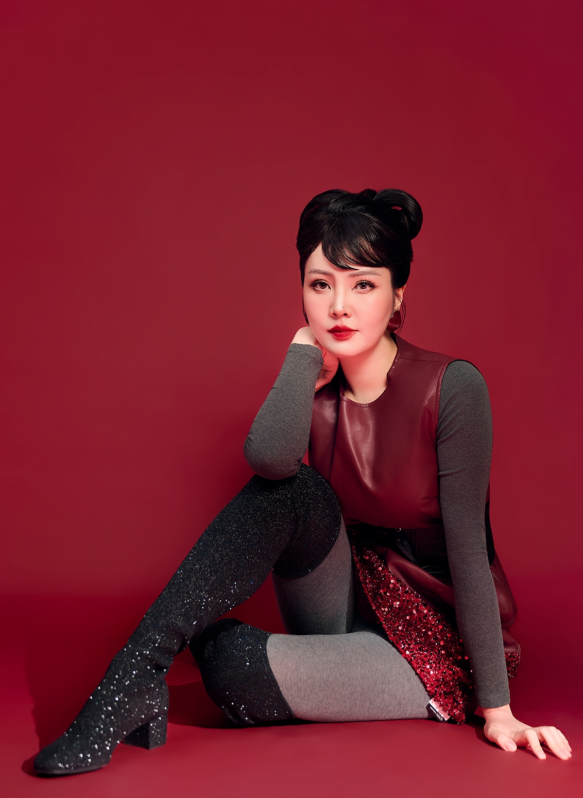 Trong khi đó, bộ ảnh thứ hai trên nền đỏ lại cho thấy một Thuỵ Vân rất khác. Không còn tư thế thẳng lưng mang tính biểu trưng cho quyền lực, cô xuất hiện trong dáng ngồi thấp, ánh nhìn trực diện, gương mặt tĩnh tại nhưng đầy chiều sâu.