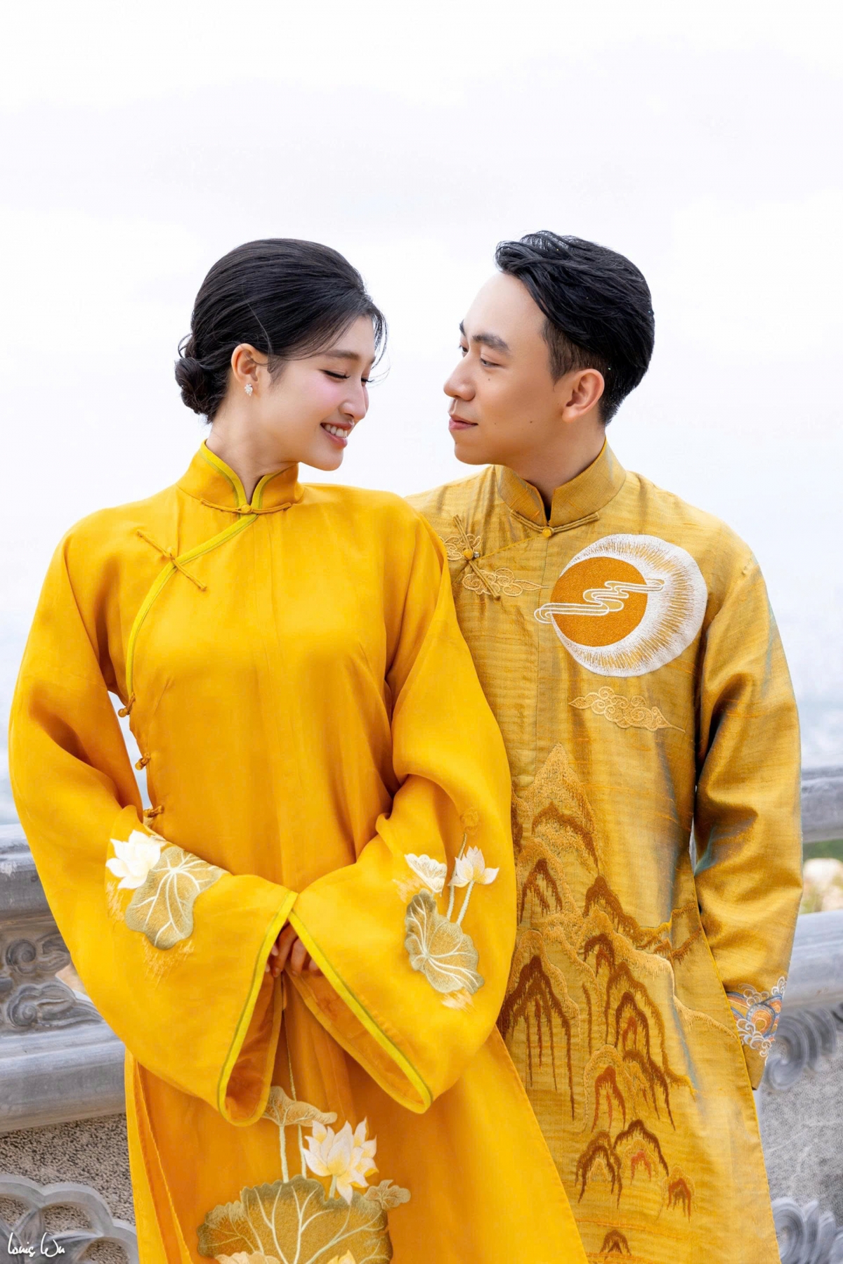 Phương Nhi diện áo dài lụa thêu hoa sen với gam vàng đồng nhã nhặn, trong khi chú rể Minh Hoàng lựa chọn áo dài thêu họa tiết mặt trời và đỉnh núi.