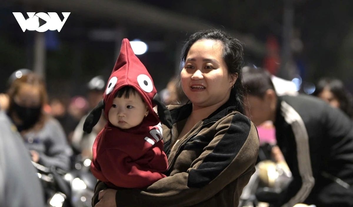 Parents lift young children onto their shoulders to watch the fireworks light up the night sky, as countdowns echo and New Year greetings fill the air.