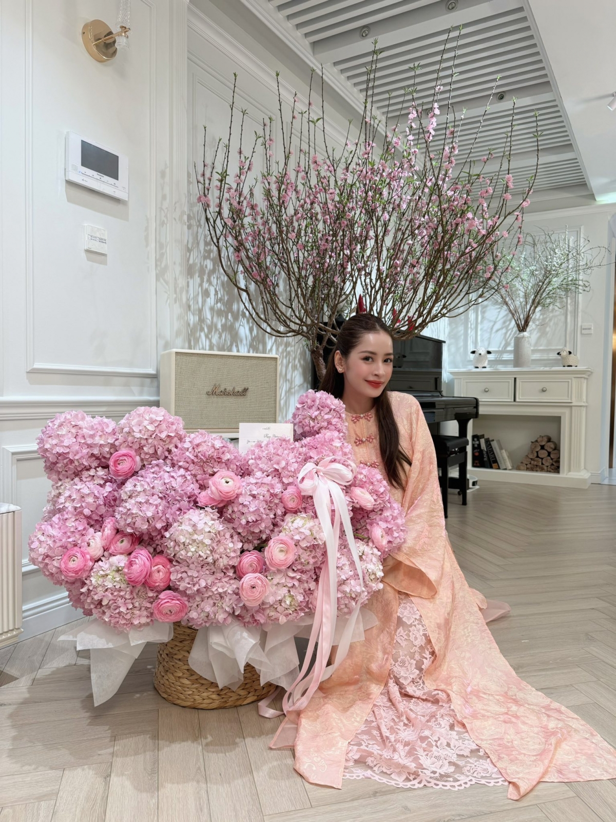 Ca sĩ, diễn viên Chi Pu biến nơi ở thành không gian xuân rực rỡ với gam màu hồng pastel làm chủ đạo. Người đẹp diện áo dài cam thêu ren, ngồi bên giỏ hoa cẩm tú cầu khổng lồ với sắc hồng phấn. Bó hoa được thiết kế hình trái tim, buộc bằng ruy băng lụa nhẹ nhàng.