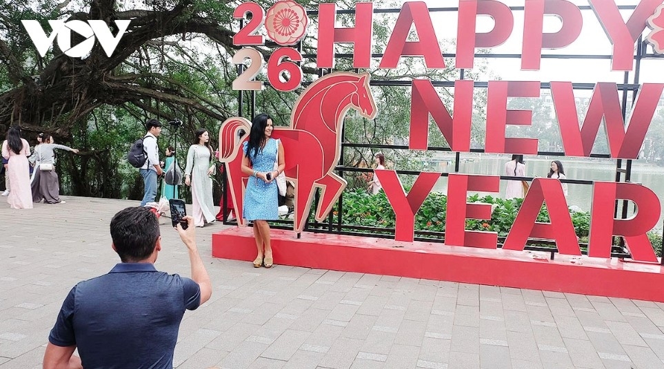 International visitors pose for photos beside the horse mascot and a “Happy New Year 2026” slogan near Hoan Kiem Lake.