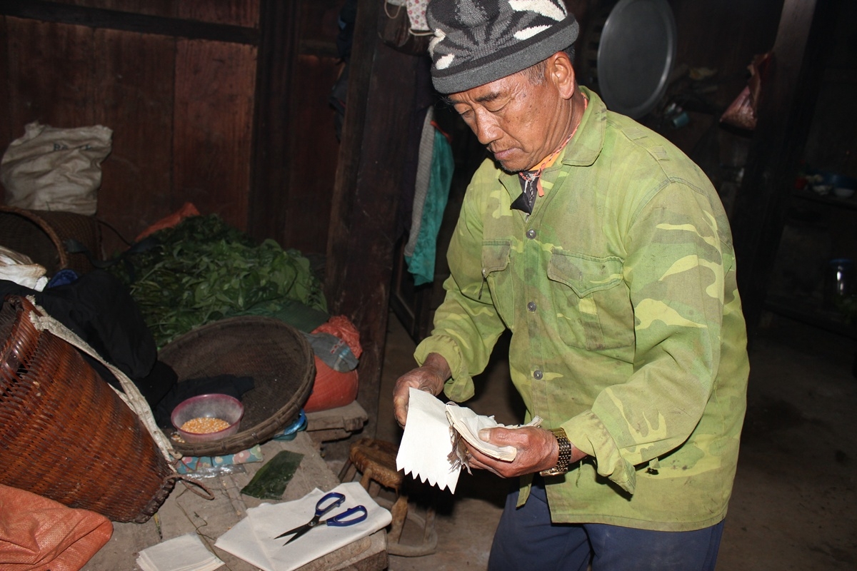 Sau khi dọn xong nhà cửa, người đàn ông chủ gia đình đồng bào Mông cắt giấy thành hình chữ nhật để dán lên những dụng cụ lao động, để công cụ lao động cũng được nghỉ tết sau một năm vất vả cùng với gia đình.