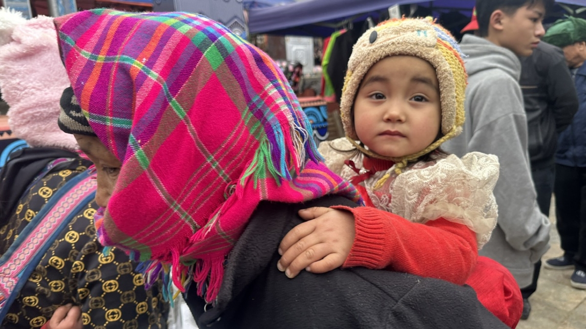 Một em bé được mẹ cõng trên lưng đi chợ Tết.