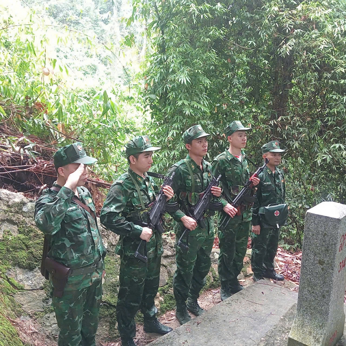 Tổ tuần tra đứng nghiêm trang bên cột mốc biên giới giữa rừng núi. Họ thực hiện nghi thức chào cờ, thể hiện tinh thần trách nhiệm, ý chí bảo vệ chủ quyền thiêng liêng của Tổ quốc.