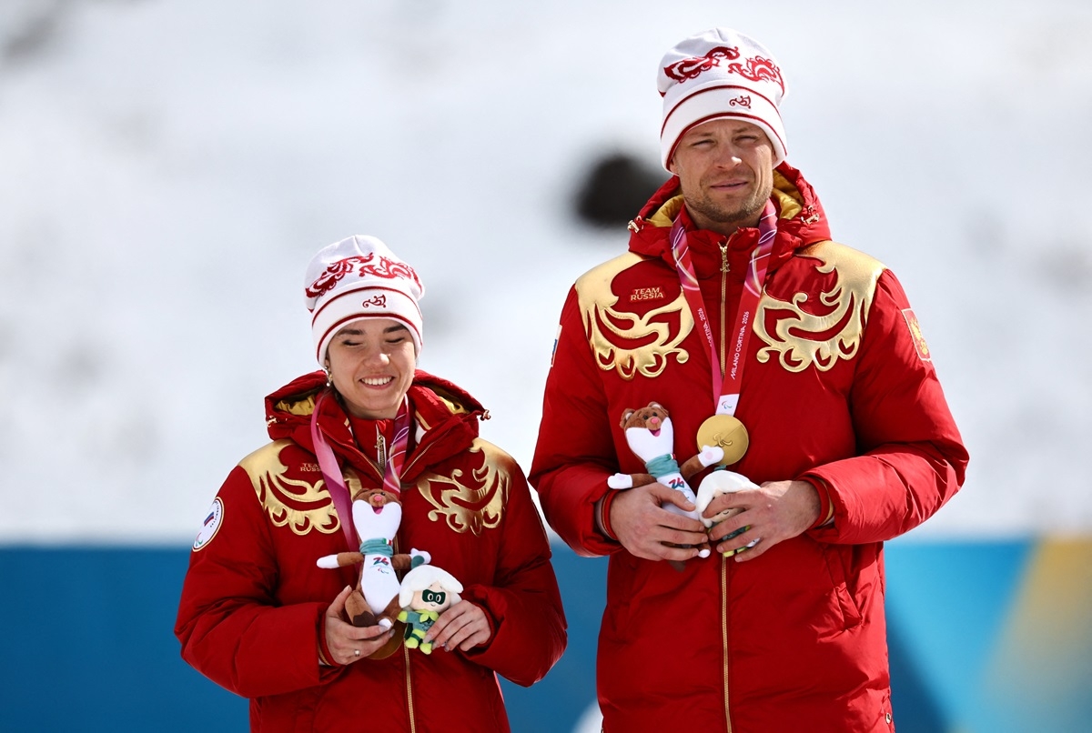 VĐV Anastasiia Bagiian và người hướng dẫn Sergei Siniakin trên bục nhận HCV tại Paralympics mùa Đông 2026. (Ảnh: Reuters).