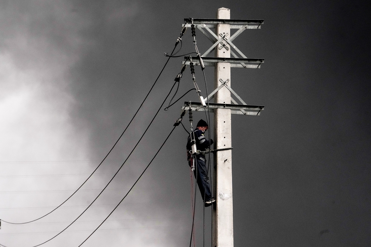Một công nhân sửa chữa điện ở Tehran ngày 8/3/2026, phía sau là cột khói đen bốc lên sau cuộc không kích của Mỹ và Israel vào cơ sở dầu mỏ của Iran. Ảnh: AP