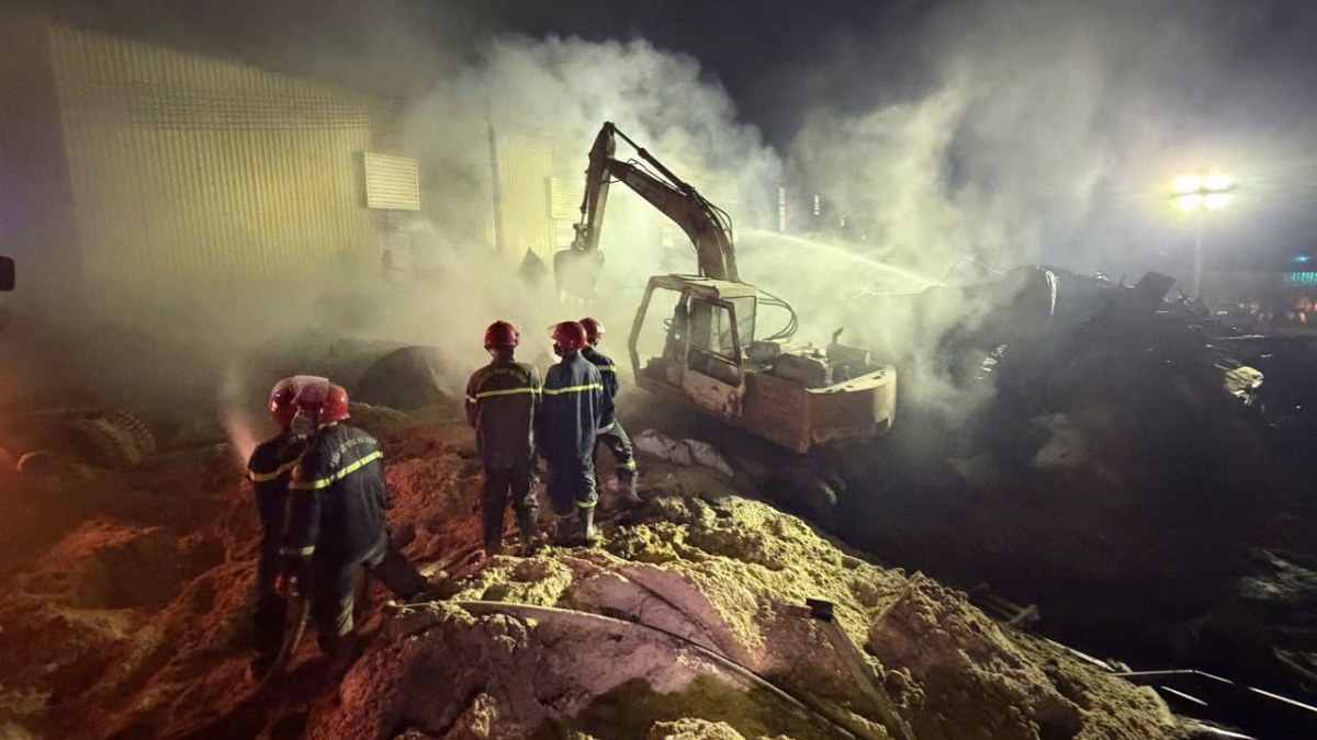 Lực lượng chữa cháy dùng máy múc xúc mùn cưa đang cháy âm ỉ để phun nước dập lửa