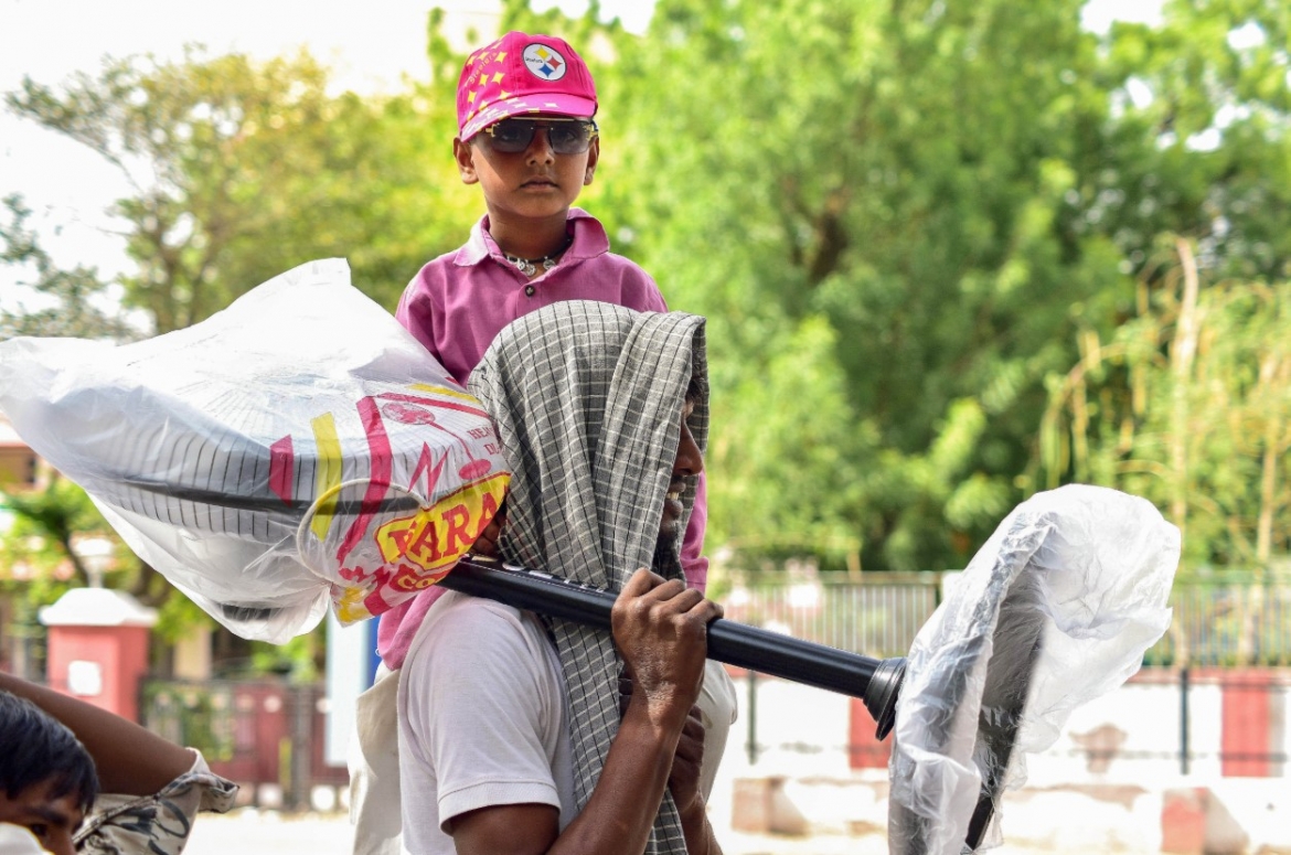 Một người đàn ông Ấn Độ địu con trên một vai và đỡ quạt đứng trên vai kia, đồng thời quàng khăn che đầu trong một ngày hè nóng nực. Ảnh: ANI