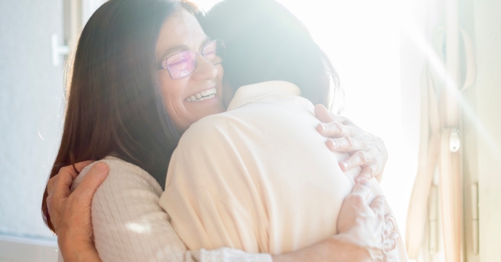 Hai người phụ nữ đang vui vẻ ôm lấy nhau. Ảnh Canva