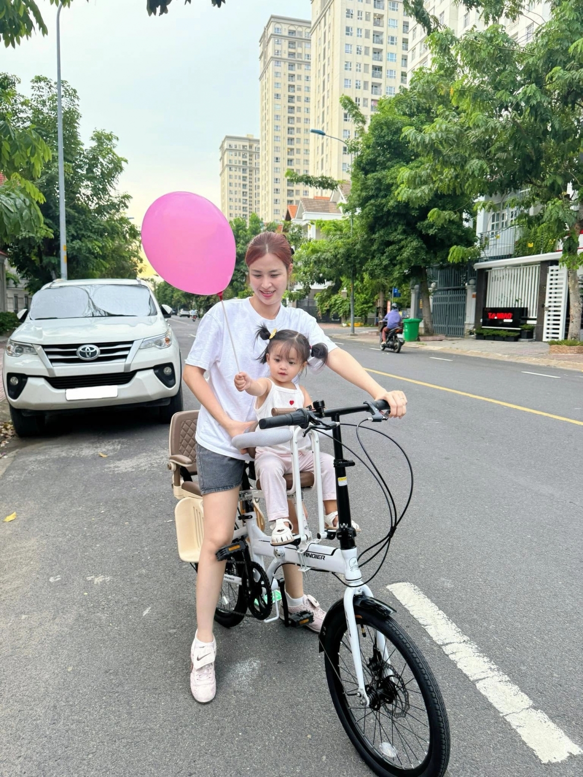 Ca sĩ Đông Nhi đạp xe chở con gái út đi dạo mát buổi chiều quanh khu phố gia đình cô đang sống.