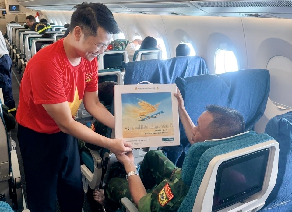 Trên chuyến bay, các tiếp viên của Vietnam Airlines mặc áo và cài huy hiệu cờ đỏ sao vàng, mang theo sắc màu Tổ quốc trong không gian khoang bay. Hình ảnh ấy hòa chung vào không khí trang trọng của hành trình, như một lời cảm ơn gửi đến các cán bộ, chiến sĩ đã hoàn thành xuất sắc nhiệm vụ và trở về trong niềm tự hào.