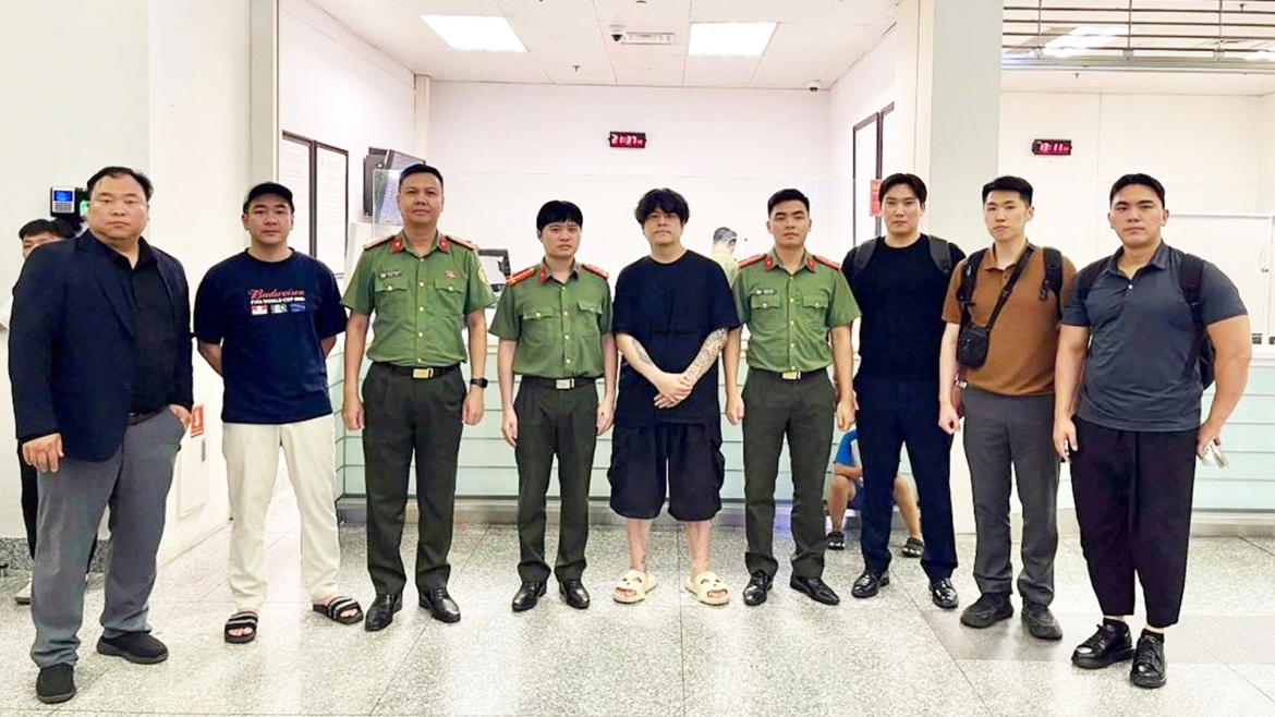 Đối tượng (áo đen quần cộc đứng giữa) được bàn giao cho phía Hàn Quốc tại sân bay Nội Bài